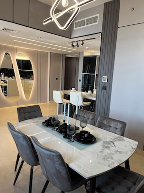 A modern dining area with a marble table, grey upholstered chairs, and contemporary lighting fixtures.