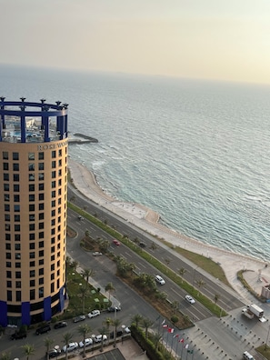 A high-rise hotel with a curved facade, a beachfront promenade, and a busy road with vehicles.