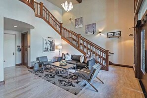A spacious living area with a wooden staircase, a sofa set, a coffee table, and a chandelier.