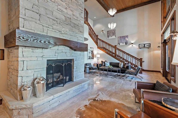 A spacious living area with a stone fireplace, a wooden staircase, and modern furniture.