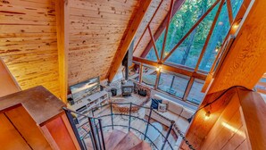 A spiral staircase in a wooden cabin with a view of the forest through large windows. - Woodsy Tahoe Cabin with Hot Tub and Deck (Carnelian Bay)