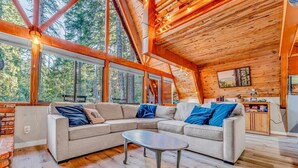 A cozy cabin interior with a large sectional sofa, a small table, and a kitchen area. - Woodsy Tahoe Cabin with Hot Tub and Deck (Carnelian Bay)