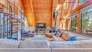 A cozy cabin interior with a spiral staircase, a large sofa, and a television in the center. - Woodsy Tahoe Cabin with Hot Tub and Deck (Carnelian Bay)