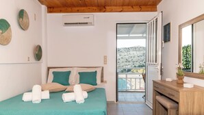 A bedroom with a bed, a wooden desk, and a balcony with a view of a hilly landscape. - Emmanouela Apartment Matala (Matala)