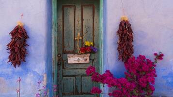A weathered blue door with a green frame, a small white lantern above, and dried flowers and vibrant pink bougainvillea in front.