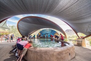 A large water feature with a semi-circular roof structure, surrounded by people. - Cat Foothills & Mountain Views / 3 BR 2 BA / Garage (Tucson)