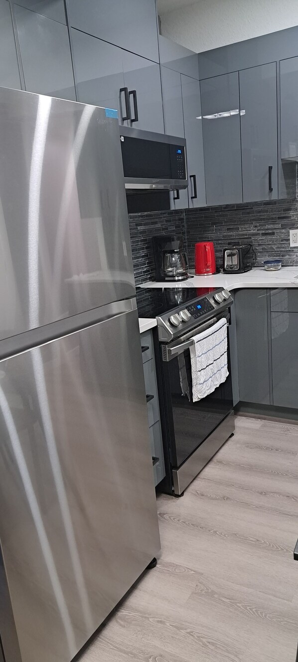 A modern kitchen with grey cabinets, a stainless steel refrigerator, a black oven, and a red kettle.