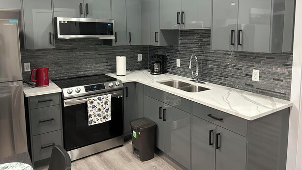 A modern kitchen with grey cabinets, a stainless steel refrigerator, a microwave, a stove, and a sink.