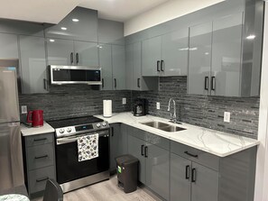 A modern kitchen with grey cabinets, a stainless steel refrigerator, a microwave, a stove, and a sink.