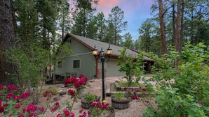 A rustic cabin with a green exterior, surrounded by a garden with vibrant flowers and a wooden bench. - *Large Groups*Sleeps 20*Must See (Flagstaff)