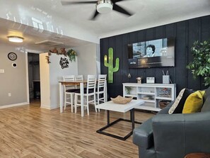 A modern living room with a dining area, a flat-screen TV mounted on the wall, and a ceiling fan. - Downtown Phoenix Triplex w/ Backyard & Free (Phoenix)