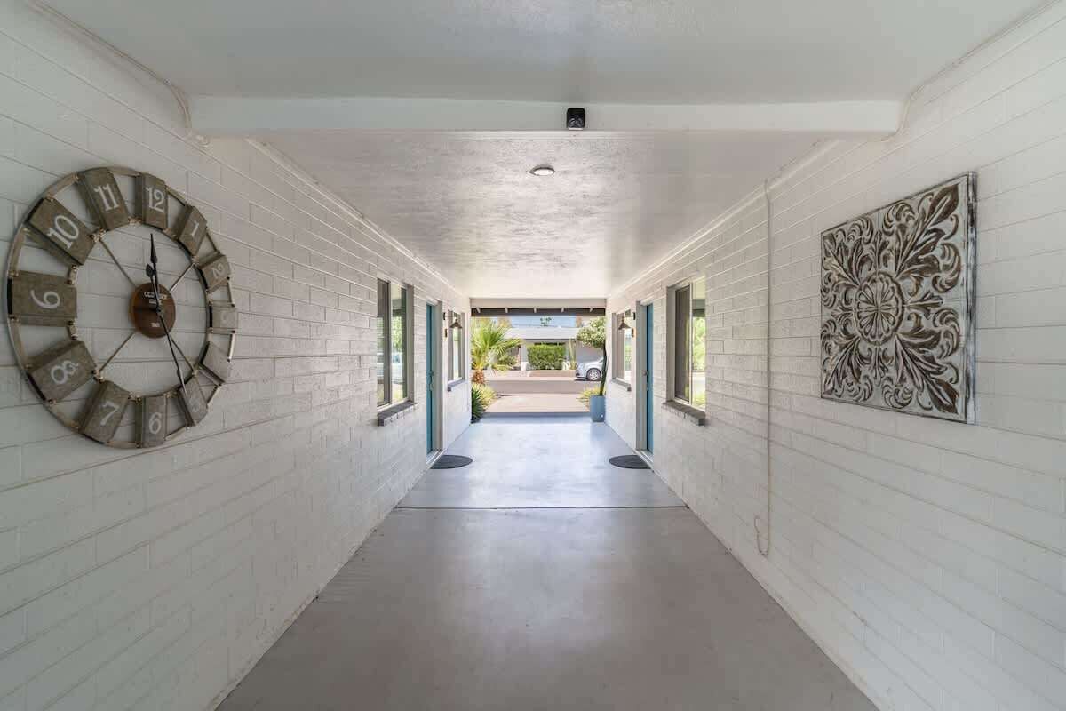 A corridor with a large clock on the left, a decorative panel on the right, and a view of the outside.