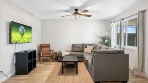 A modern living room with a sectional sofa, a coffee table, a TV, and a ceiling fan.