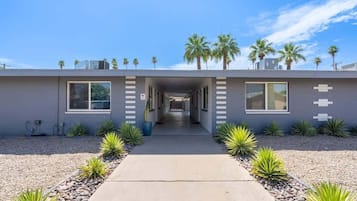 A modern building with a central corridor, palm trees on the roof, and a gravel pathway.