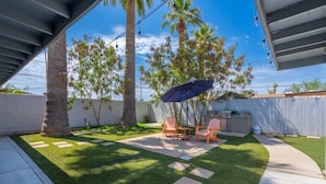 A backyard with artificial grass, a patio table, chairs, and an umbrella.