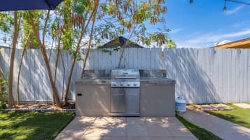 An outdoor kitchen with a grill, a gas tank, and a wooden fence in the background.