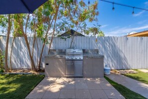 An outdoor kitchen with a grill, built-in oven, and a gas tank.