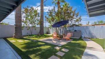 A backyard with artificial grass, a patio table, chairs, and an umbrella.