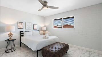 Ein Schlafzimmer mit einem Bett, einem Deckenventilator, einem Fenster mit Jalousien und Kunstwerken an der Wand.