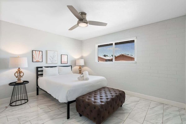A bedroom with a bed, a ceiling fan, a window with blinds, and artwork on the wall.