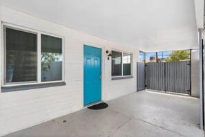 A white building with a blue door, a grey fence, and a concrete patio.