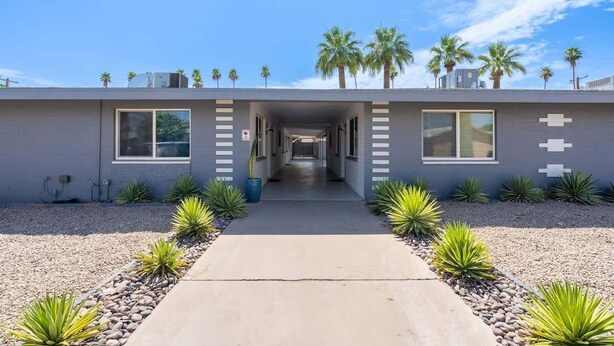 A modern building with a central corridor, palm trees on the roof, and a gravel pathway.