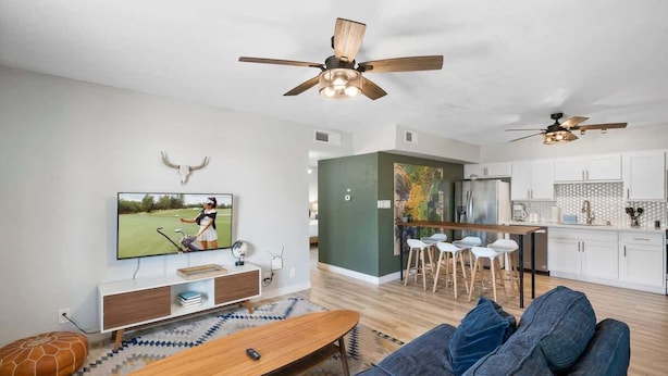 A modern living room with a television, sofa, and wooden coffee table. There is a kitchen area with white cabinets and a dining space with stools. - Chic Scottsdale Apt 2 |FashionSquare|OldTown|4Plex (Scottsdale)