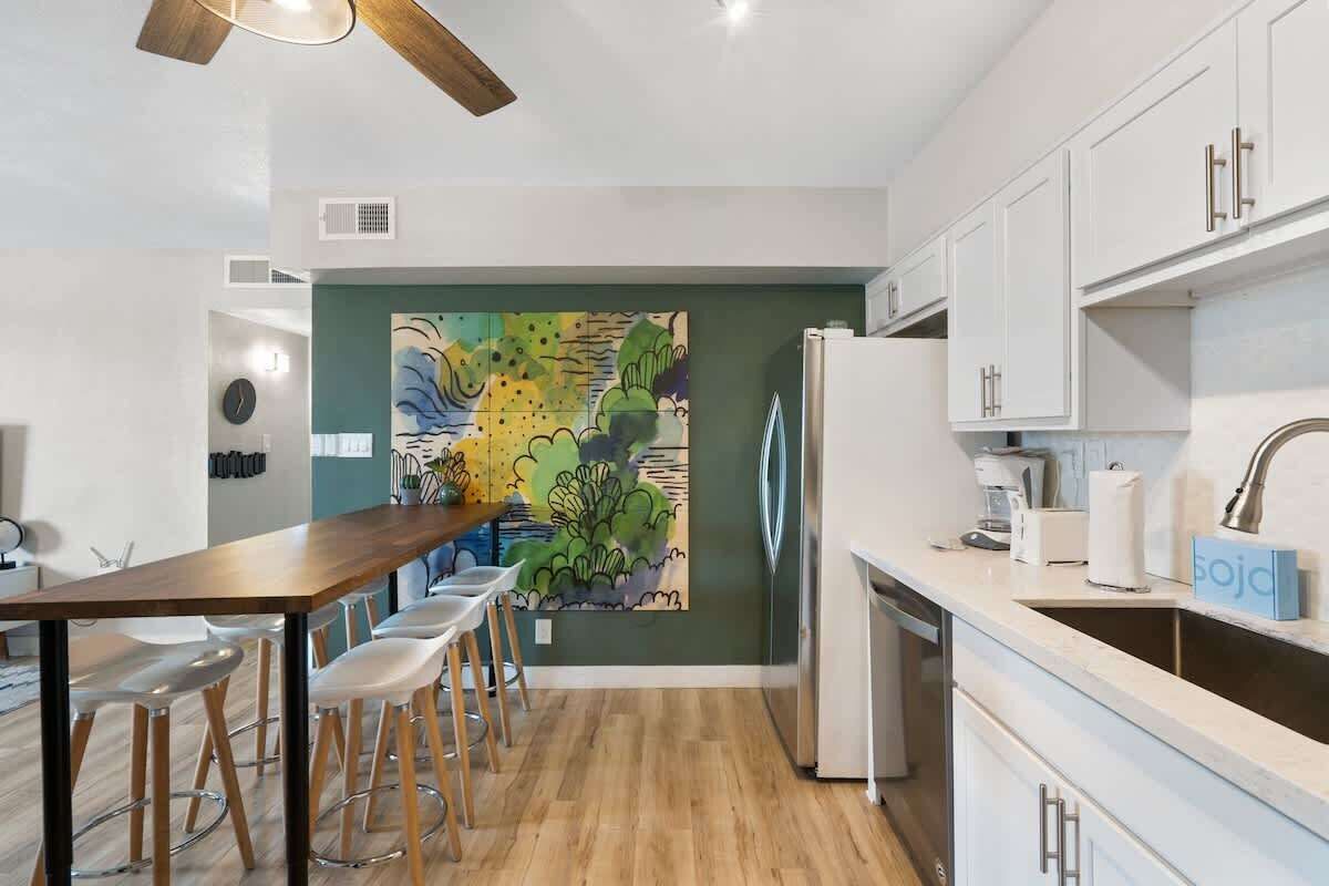 A modern kitchen with a wooden dining table, bar stools, a refrigerator, and a sink.