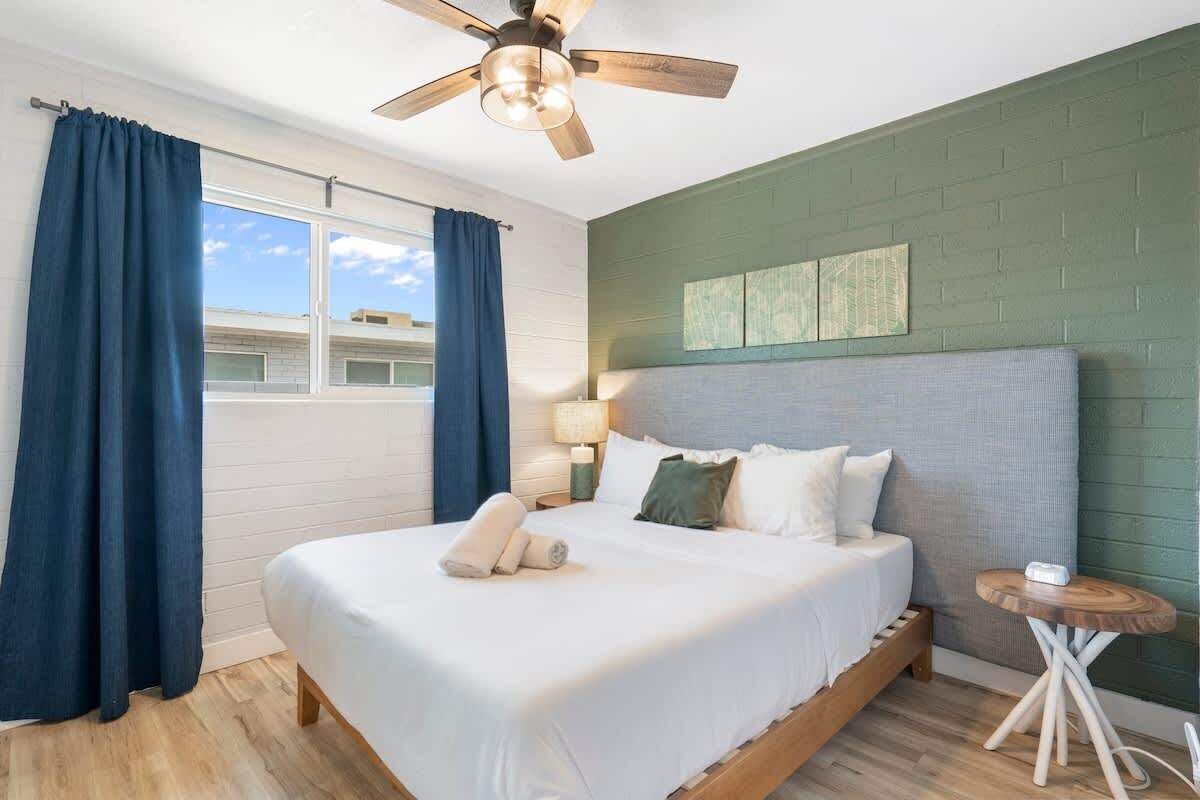 A bedroom with a bed, a ceiling fan, a bedside table, and a window with curtains.