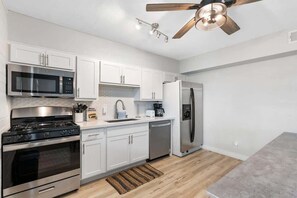 A modern kitchen with white cabinetry, stainless steel appliances, and a wooden ceiling fan. - Chic Scottsdale Apts 1-4|FashionSquare|OldTown (Scottsdale)