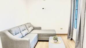 A modern living room with a grey sectional sofa, a small white coffee table with a plant, and a window with grey curtains.