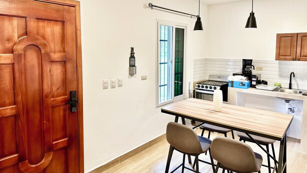 A compact kitchen with a wooden door, a small dining table with chairs, and pendant lights.