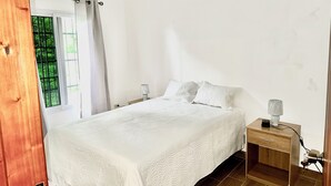 A bedroom with a bed, two bedside tables, a nightstand, a lamp, and a window with curtains.