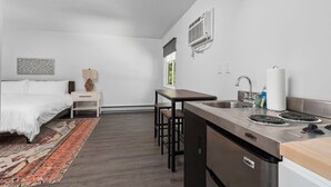 A compact hotel room with a bed, bedside table, lamp, and a small kitchenette with a stove and sink. - Peninsula One unit 18 Close to downtown and beach (Traverse City)