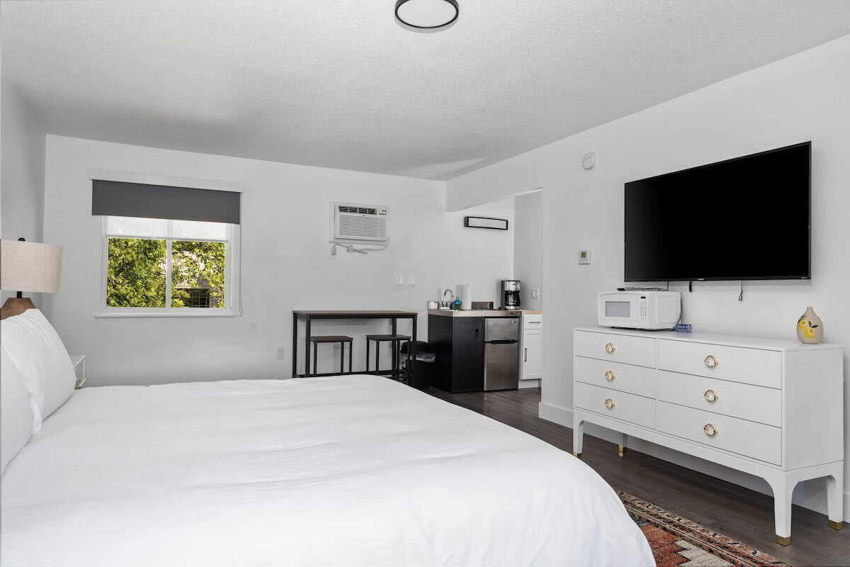 A bedroom with a large bed, a TV, a dresser, a desk, and a window.