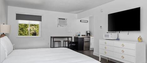 A bedroom with a large bed, a TV, a dresser, a desk, and a window.