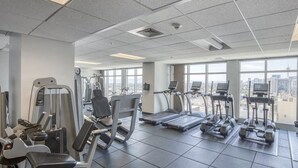 A gym with cardio machines, weight machines, and a view of the city through large windows.