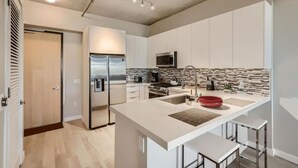 A modern kitchen with white cabinetry, a stainless steel refrigerator, a microwave, a sink with a red bowl, and a tiled backsplash. - Sparkling Juhl byFremont-1 queen 1 sofa bed TONS of Amenities (Las Vegas)