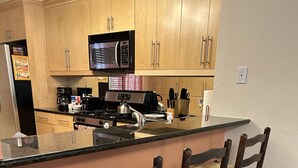 A kitchen with wooden cabinets, a microwave, a stove, and a bar area with four wooden barstools. - Meridian by Strip 6ppl Amenities 2Qu&sofa kids ok (Las Vegas)