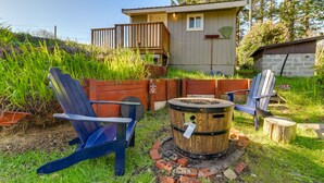 A rustic outdoor seating area with Adirondack chairs, a wooden barrel fire pit, and a wooden deck. - Fish On-Site & Explore Coos Bay! Creekfront Cabin (Coos Bay)