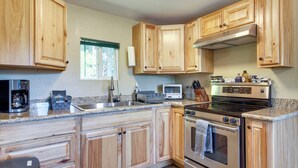 A kitchen with wooden cabinets, stainless steel appliances, granite countertops, and a window with a view of greenery. - Fish On-Site & Explore Coos Bay! Creekfront Cabin (Coos Bay)