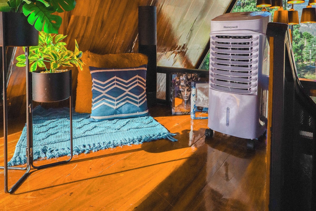 A cozy room with a wooden ceiling, a Honeywell air conditioner, a blue patterned cushion, and a potted plant.