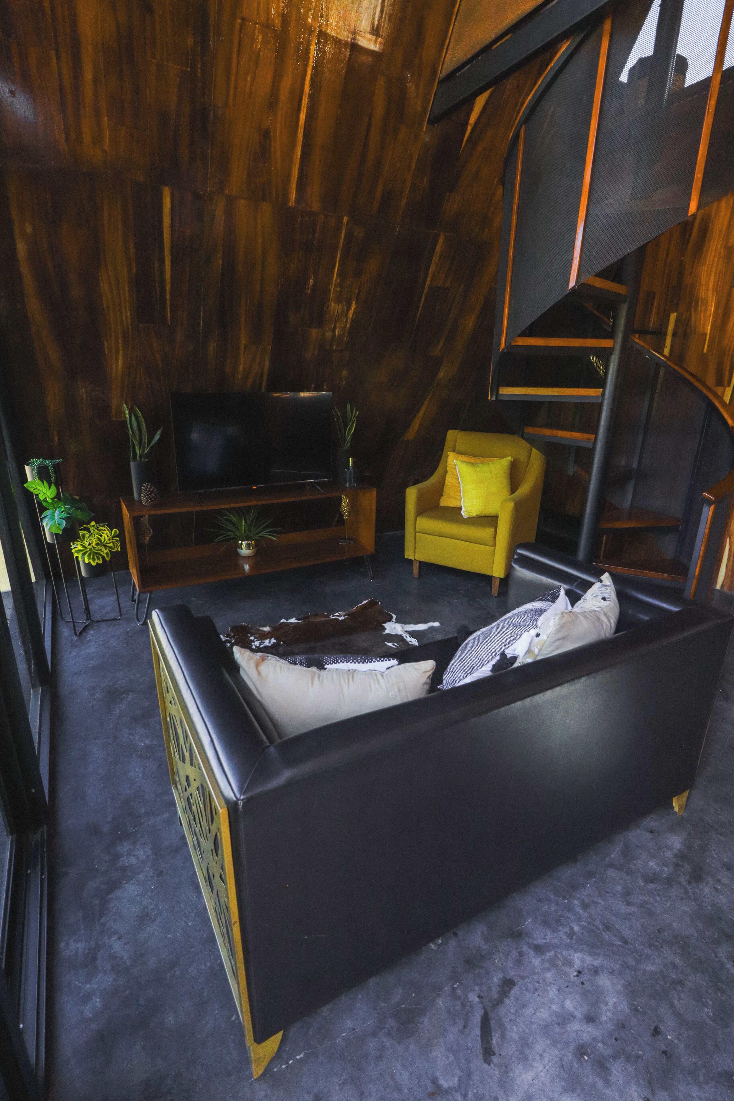 Une pièce avec un lit, un fauteuil jaune, un téléviseur posé sur un meuble en bois et un escalier.