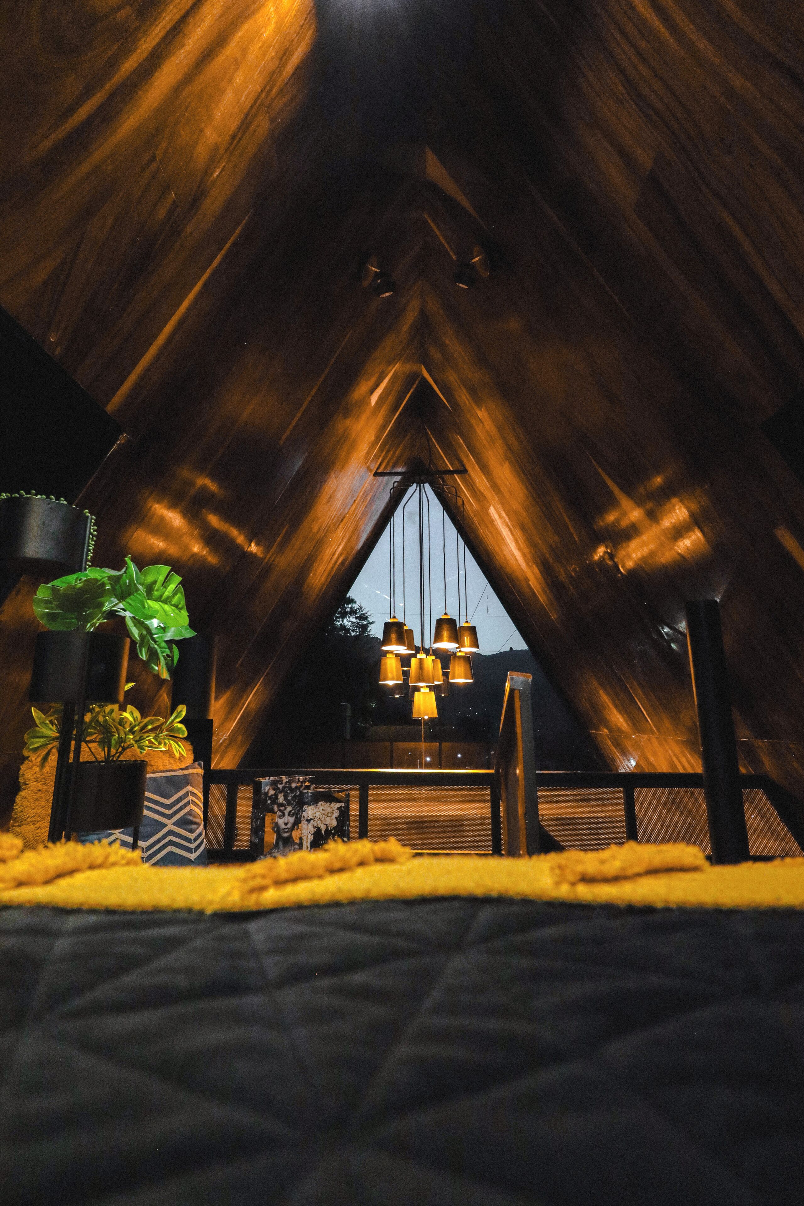 An attic room with a sloped ceiling, hanging pendant lights, and potted plants.