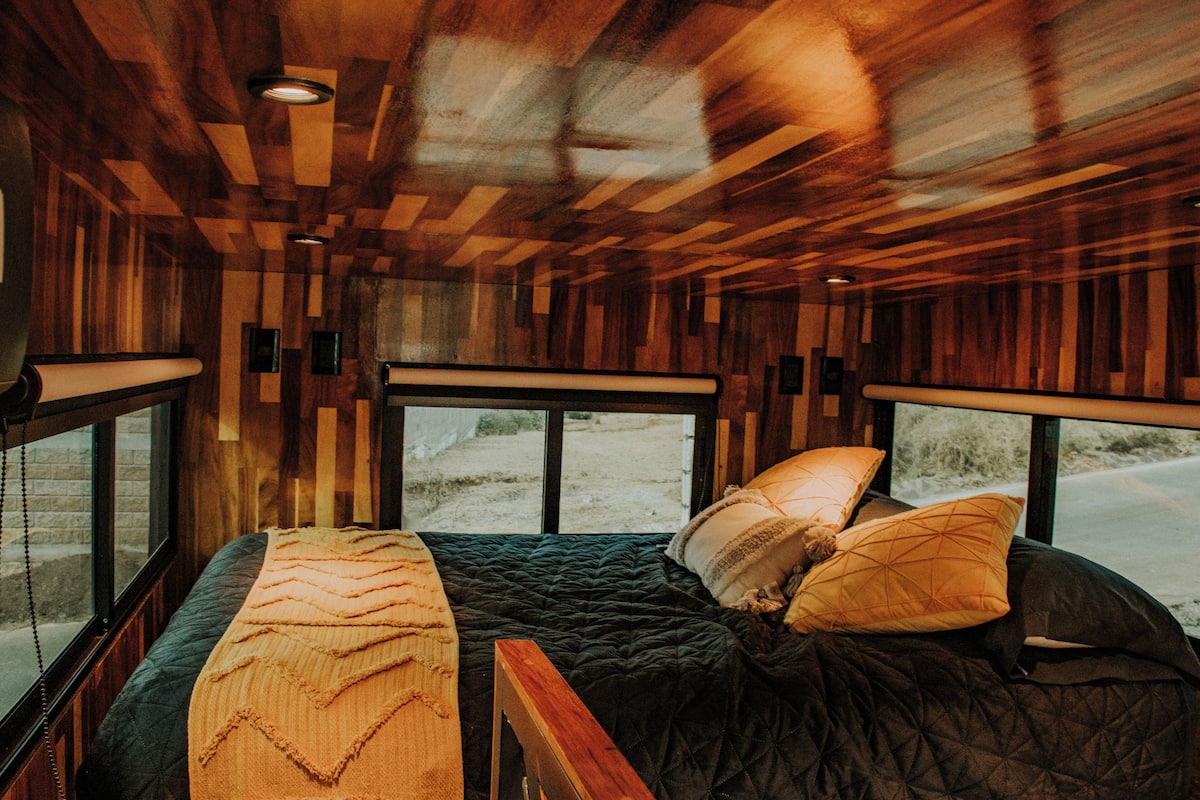 A room with a bed, large windows, and wooden paneling on the ceiling.