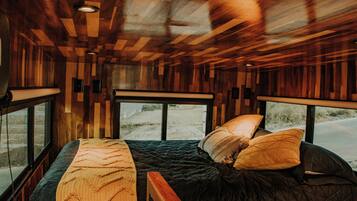 Una habitación con cama, ventanas amplias y paneles de madera en el techo.