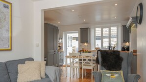 Una cocina moderna con armarios grises, un comedor con mesa y sillas de madera, y una sala de estar acogedora con sofá gris y cojines decorativos.