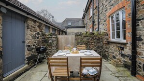 Un edificio de piedra con un patio techado, una mesa lista para comer y una parrilla.