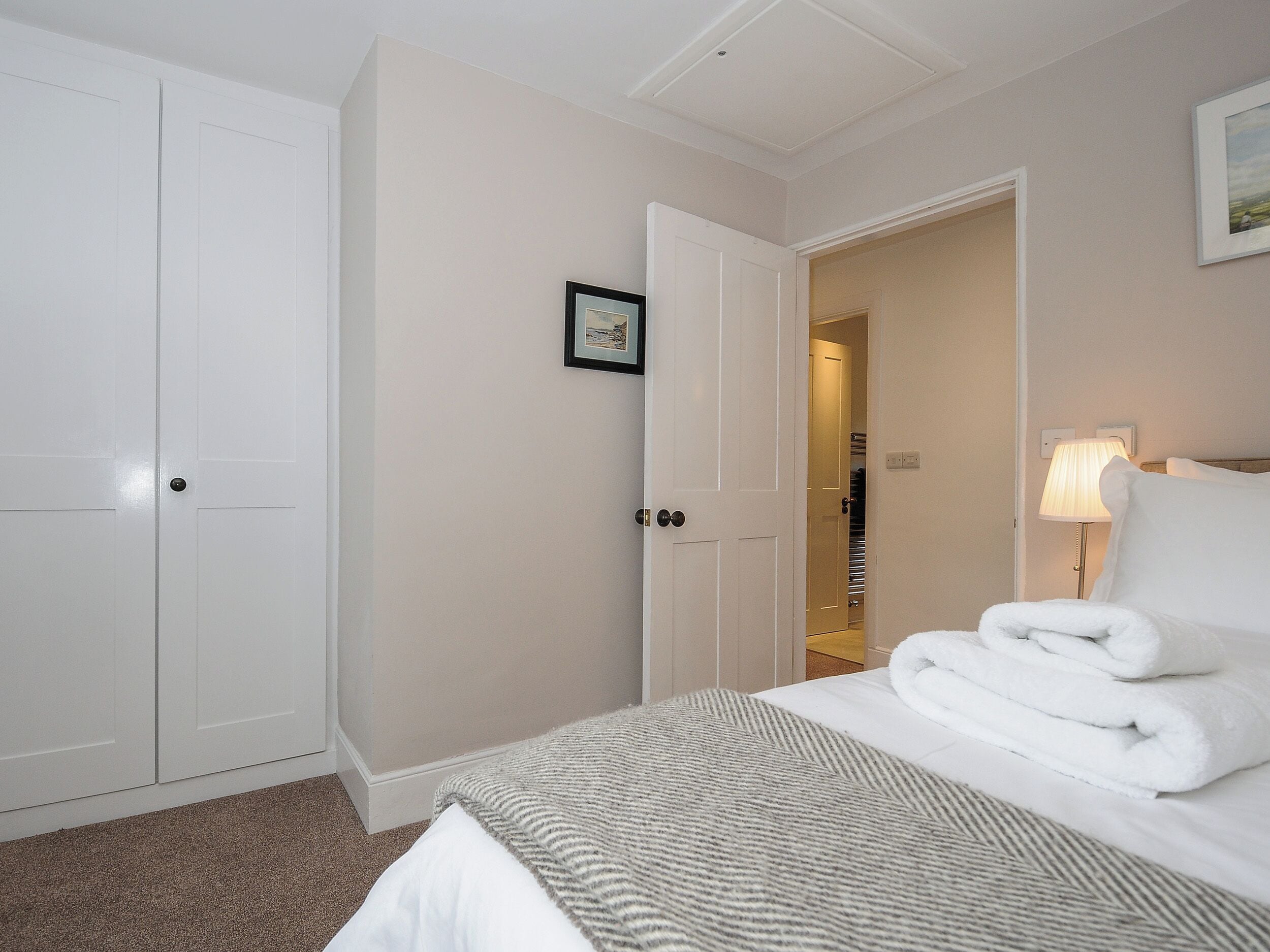 A hotel room with a bed, a bedside lamp, a door, and a framed picture on the wall.