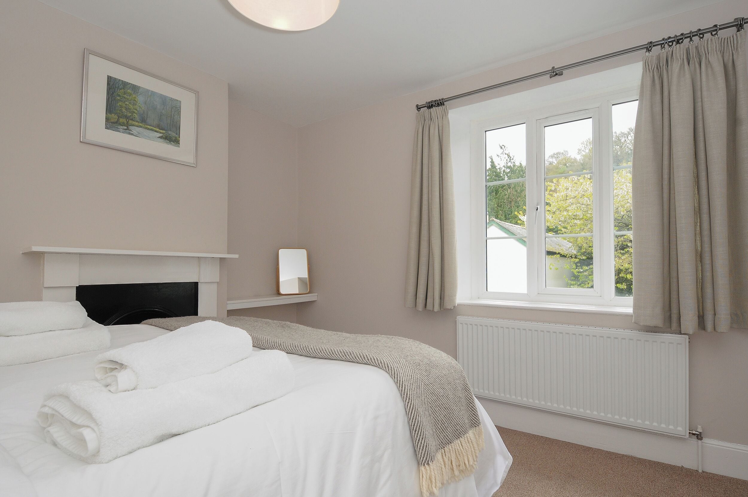 A bedroom with a bed, a fireplace, a window with curtains, and a framed picture on the wall.